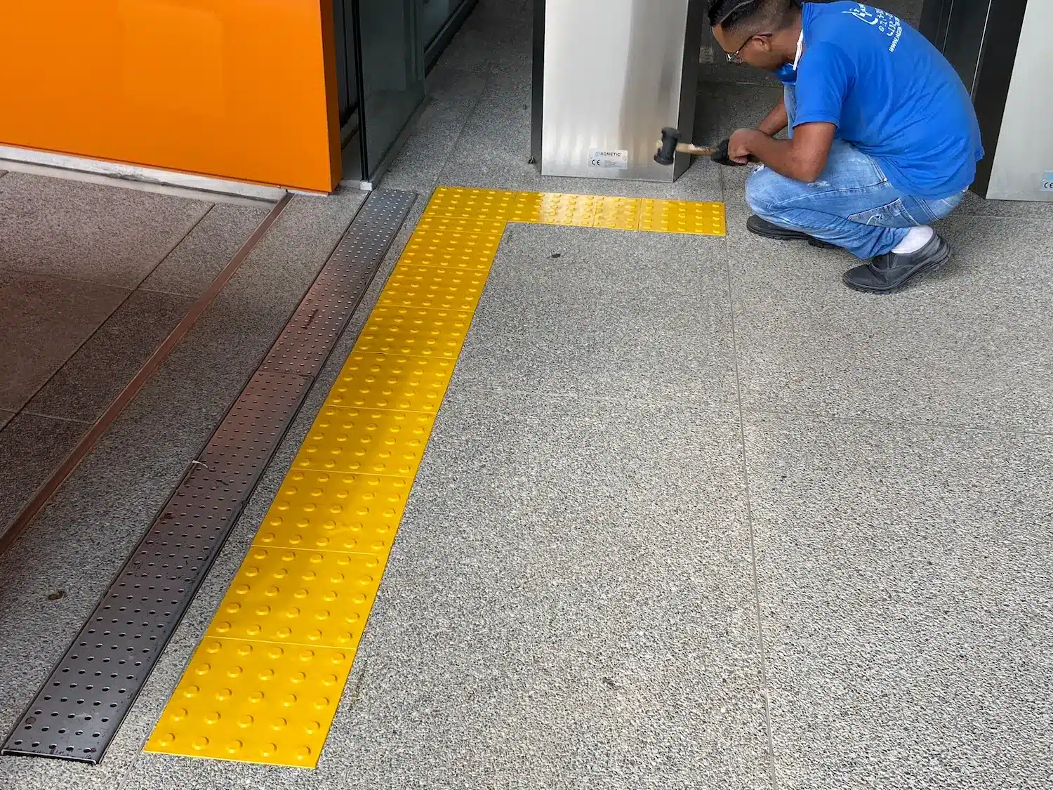 Profissional usa martelo de borracha enquanto mostra como instalar piso tátil da cor amarela no chão
